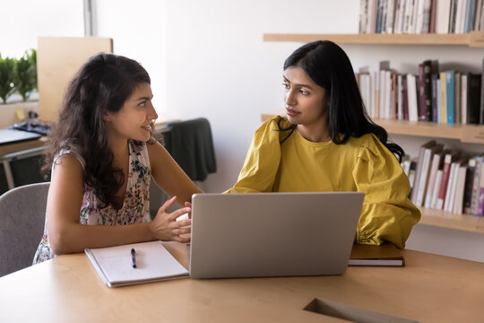 Peer mentorship. Smart young girl college university student support help female groupmate in learning research teach to use education app on notebook pc at library share idea at self preparation time