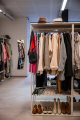 Clothing rack with jackets, sweaters, and accessories in thrift store. Shoes and scarves neatly...
