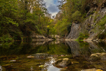 Fototapeta premium Reflections of rocks, trees and sky in the calm waters of a river