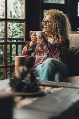 Mature woman sitting alone at home holding a cup of hot herbal tea while looking around with a...