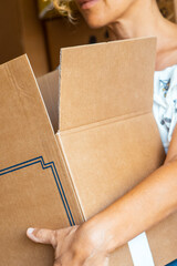 A woman lifting a large cardboard box in her home, wearing casual clothing, with scattered...