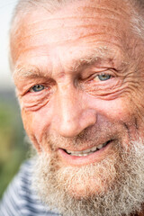 Portrait of an elderly man in retirement, enjoying peaceful moments outdoors, smiling contently, showing physical and mental wellbeing, wearing casual clothes, close-up with wrinkles, gray hair, blue