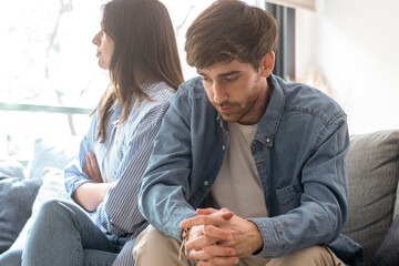 Unhappy couple sitting on a couch at home, avoiding eye contact, engaged in a tense discussion about marriage issues, trust problems, emotional detachment, financial difficulties, and separation
