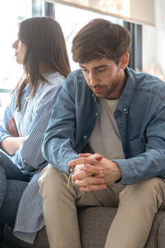 Unhappy couple sitting on a couch at home, avoiding eye contact, engaged in a tense discussion about marriage issues, trust problems, emotional detachment, financial difficulties, and separation