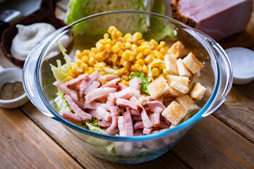 A large bowl of salad with ham, corn and Peking cabbage on a wooden table. Close-up