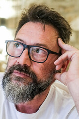 In a quiet room at home, a 50-year-old man with glasses sits alone, his face marked by sadness and concern, as he struggles with feelings of loneliness, emotional exhaustion, and personal worries