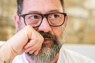 An adult male, around 50 years old, is sitting indoors in a living room, wearing glasses and...