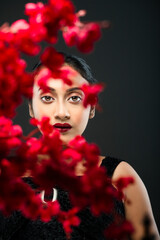 face of a beutiful female model behind a bunch of red flowers shot in a studio in front of a black background