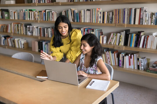 Student mentorship. Two young girls university scholars peers work on collaborative project use notebook in modern library. Female scientist expert guide colleague in research share experience skills