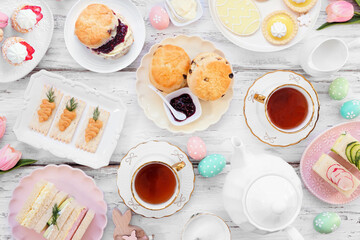 Easter or spring tea table scene against a white wood background. Selection of finger sandwiches,...