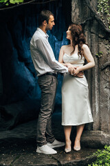couple standing next to each other. The background of the photo is a stone wall partially covered with greenery.