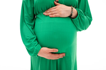 Close-up image of pregnant woman in green dress holding hands near belly, expecting baby. Symbol of...