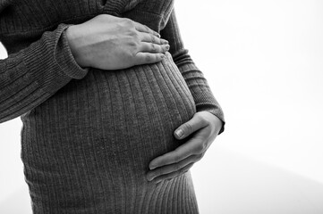 Close-up image of pregnant woman's belly, holding hands near belly, waiting for baby. Symbol of...