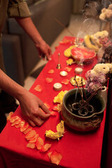 Person arranging flowers and incense on an altar with dedication, petals scattered around enhancing spiritual ambiance creating calm atmosphere