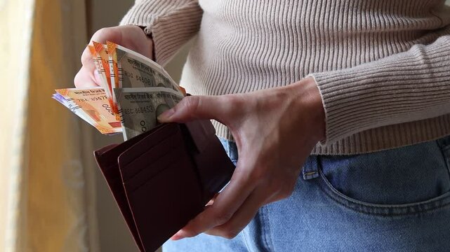 Woman's hands holding leather wallet with brand new indian 100, 200, 500 rupees INR banknotes. Concept of saving money, cash settlement, financial literacy and planning.