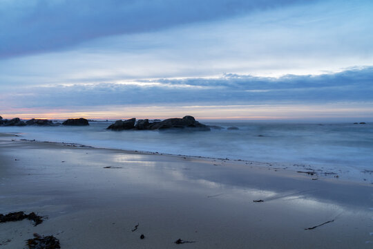 Rochers dispers&eacute;s sur la plage de Kerlouan, entour&eacute;s d&rsquo;une mer soyeuse gr&acirc;ce &agrave; la pose longue. Le ciel d&rsquo;hiver offre un tableau d&eacute;licat aux tons bleus et roses.