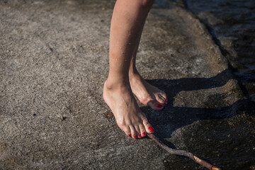 Bare feet of woman sitting on a rock next to sea water, sensorial reflexology