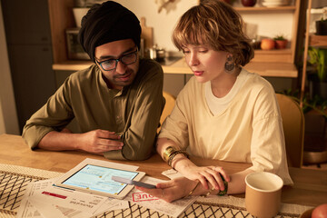 Fototapeta premium Concentrating on financial planning with use of digital tablet and paperwork at cozy wooden table. Discussing strategies on budgeting and savings, focusing on effective financial management