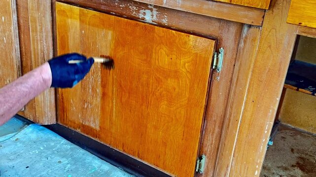 A person applies a new shellac finish to wooden cabinets.