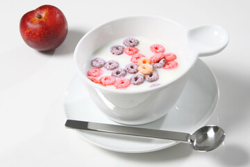 Colorful cereal rings floating in milk, modern spoon alongside ripe plum, presenting vibrant morning nutrition
