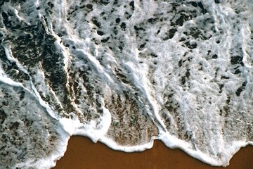 Fototapeta premium Textured Background. Sea foam splashed on the shore. Top view. Abstract composition. Sand. Waves. Postcard. Cover. Picture. Wallpaper. Close-up