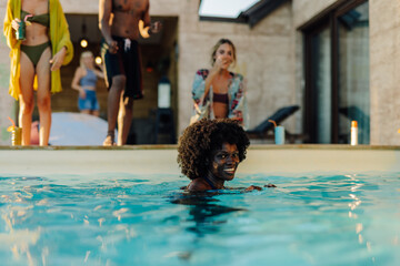 Young woman swimming in a pool during a summer party with friends