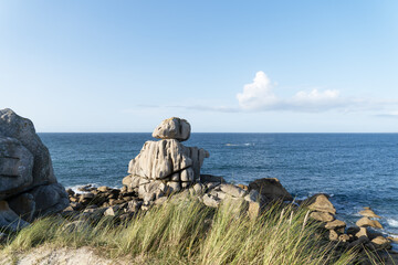 Paysage maritime aux Amiets &agrave; Cl&eacute;der : rochers sculpt&eacute;s par les vagues, mer d&rsquo;azur et oyats verdoyants sous un ciel bleu anim&eacute; de nuages blancs.
