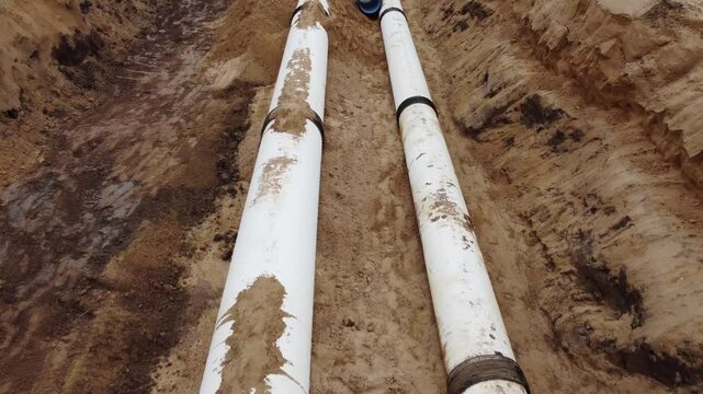 Two pipes are laying in the dirt, one of which is bent. The other is straight. The bent pipe is in the middle of the two