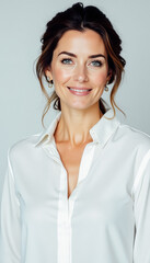 Fototapeta premium Woman with dark brown hair in a white blouse, smiling warmly in a soft-lit studio.