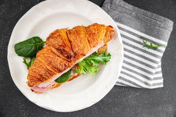 Croissant sandwich ham, cheese, green leaf salad delicious gourmet food background on the table rustic food top view copy space
