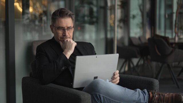 Businessman using laptop computer in office lobby or on cafe terrace. Happy middle aged man, entrepreneur, small business owner working online. - Powered by Adobe
