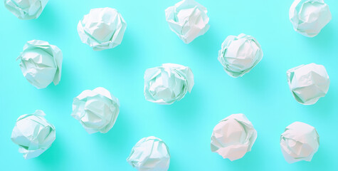 Naklejka premium Crumpled white paper balls are randomly arranged on a vibrant turquoise background, creating an artistic flat lay appearance