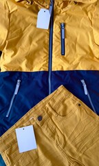 Label on clothes. New orange jacket with white price tag and mustard colored trousers. Fragment of jacket with label, zipper, zippered pocket. Sewing clothes, production and sale of things