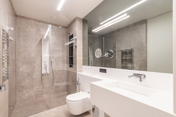 Modern design of the bathroom, decorated in beige tones. Sensory shower behind a glass partition....