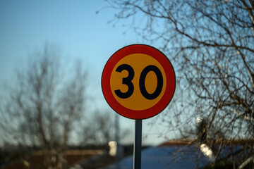 A clear blue sky serves as a backdrop for a vibrant speed limit sign displaying 30 km/h. Nearby,...