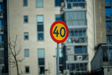 A bright speed limit sign marked with 40 can be seen prominently in an urban setting, with modern buildings in the background under clear blue skies