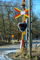 Brightly colored railroad crossing signals stand tall beside a quiet road during winter. The...