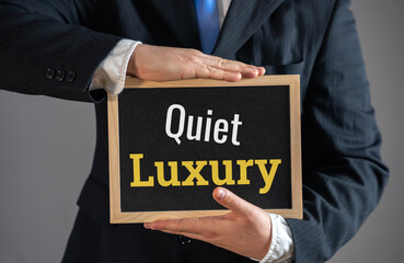 A businessman holds a sign Quiet Luxury. High-end minimalism. Refined wealth, exclusive branding, and premium lifestyle choices. Don't give the appearance of being ultra-rich. Modesty and practicality