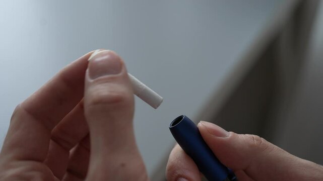 Male inserting tobacco stick into sleek iqos device, closing carefully and storing compact charger. Concept of heat-not-burn smoking alternative for modern nicotine consumption, close-up, slow motion.