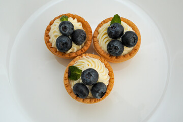 Delicious blueberry cupcakes with white chocolate cream on a white plate on a white background. Beautiful cake decoration.
