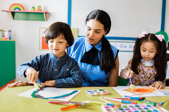 Teacher and children painting in art class at kindergarten daycare. Multiracial kids have fun at school classroom. Preschool education concept