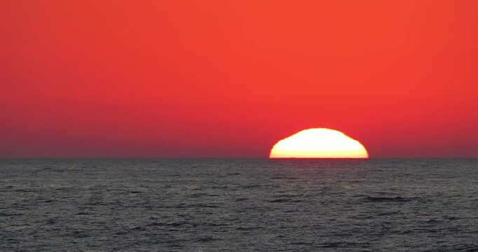 Big bright sun on red sky going down under the sea level at horizon on sunset, ultra zoom fast motion timelapse