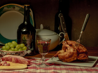 A stylized antique still life with a grilled chicken, a glass of red wine and lard.