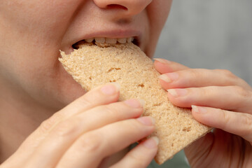A close-up of a woman biting into a whole grain cracker.