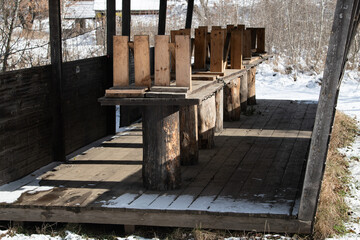 Snow covers the ground around an empty wooden pavilion, featuring sturdy benches and a rustic atmosphere. The landscape reflects the quiet tranquility of winter in a rural area