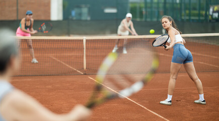 Fototapeta premium Young and elderly women doubles play against women in tennis on court