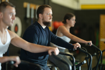 Willing young man engaged in air-bike workout in exercise room during weight training classes