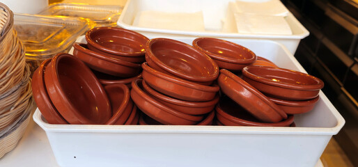 Stacked terracotta dishes in a white plastic container; wicker basket on the left; clear plastic trays and white napkins in the background;