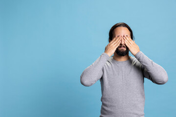 Young adult showing the three wise monkeys symbol with hands over his eyes, covering eye sight to...