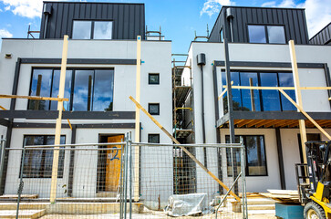 A modern, two-story residential townhouse building under construction. The scaffolding and building...